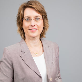 Frau mit kurzem Haar und Brille in hellem Blazer vor neutralem Hintergrund