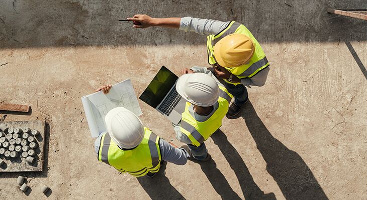 Drei M&auml;nner in Warnweste und Helmen; einer zeigt in eine Himmelsrichtung, alle anderen schauen in gezeigte Richtung. 