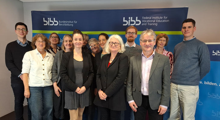 Gruppe von Teilnehmenden steht vor zwei blauen Bannern mit dem Logo und Schriftzug des Bundesinstituts f&uuml;r Berufsbildung.