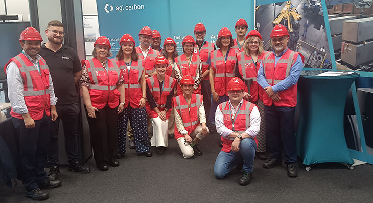 15 people wearing high-visibility vests and helmets are standing in front of a promotional wall bearing the inscription ‘sgl carbon’.