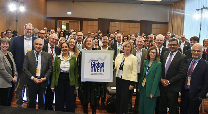 Gruppe von Personen steht in einem Konferenzraum hinter einem Schild mit der Aufschrift 'Global TVET'.