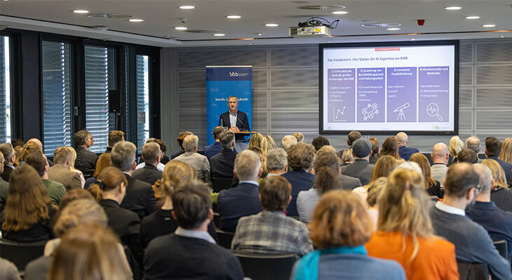 Gruppe von Personen in einem Raum, die sich vor einem Tisch mit Pflanzen unterhalten.