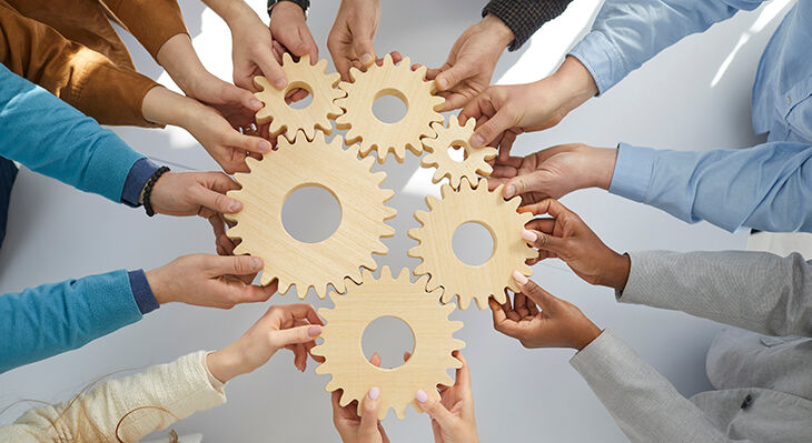 Hands of office workers holding wooden gears that symbolize coordinated teamwork