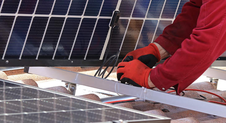 Installierung eines blauen Solarpanel. Man sieht das Panel im Hintergrund. Im Vordergrund zwei Arme in roter Fleecejacke und rot-schwarze Handschuhe. 