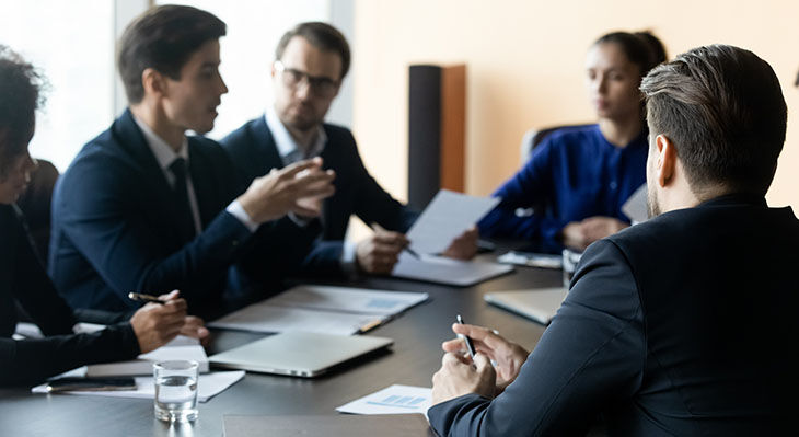 M&auml;nner und Frauen in Anz&uuml;gen sitzen an einem Tisch.