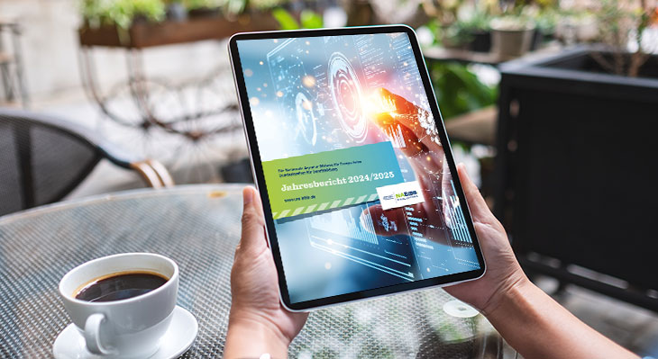 Person h&auml;lt Tablet mit digitaler Anzeige des Jahresberichts 2024/2025 vor einem Tisch mit Kaffeetasse