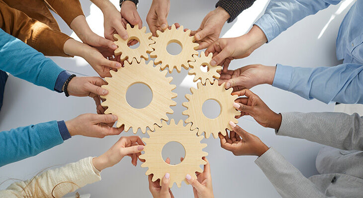 Hands of office workers holding wooden gears that symbolize coordinated teamwork