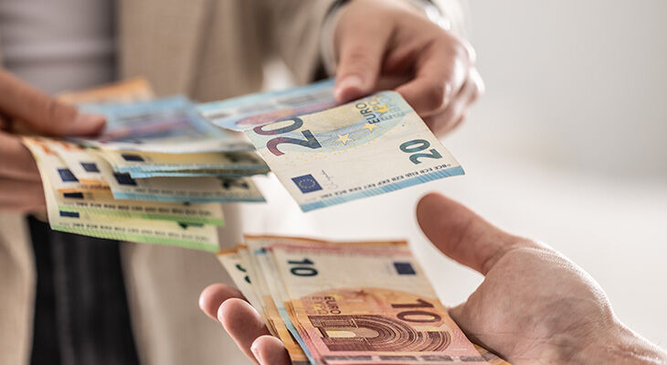 Zwei H&auml;nde tauschen mehrere Euro-Banknoten in verschiedenen St&uuml;ckelungen aus