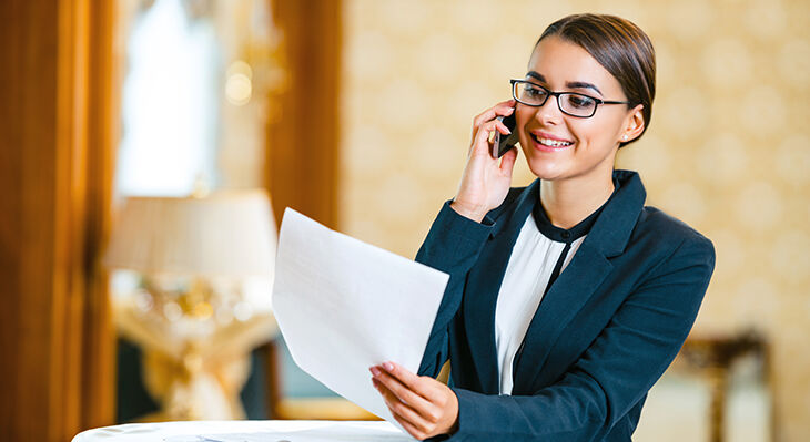 Eine Frau telefoniert mit einem Blatt Papier in der Hand.