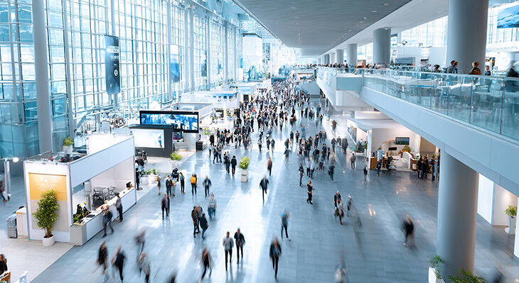 Gro&szlig;e, helle Eingangshalle mit vielen Menschen, Glasgel&auml;ndern und moderner Architektur