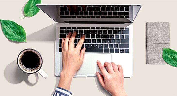 H&auml;nde, die auf offener Laptoptastatur liegen; daneben eine Kaffeetasse und 3 gr&uuml;ne Bl&auml;tter (Vogelperspektive)