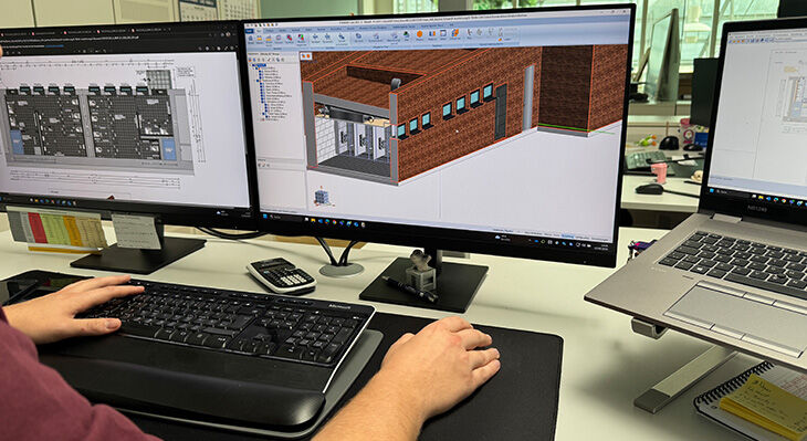 Die Hände eines angehenden Bautechnischen Konstrukteurs arbeiten an Tastatur und Maus, auf den zwei Bildschirmen vor ihm sieht man Baupläne und Modelle