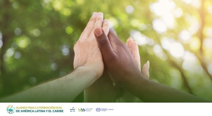 H&auml;nde unterschiedlicher Hautfarbe ber&uuml;hren sich mit gespreizten Fingern vor unscharfem, gr&uuml;nem Hintergrund.