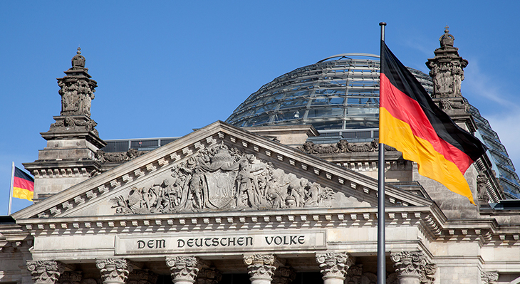 Nahaufnahme vom Reichstagsgebäude in Berlin mit Deutschlandfahne im Vordergrund