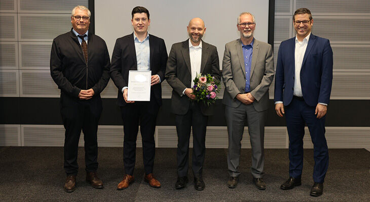 F&uuml;nf M&auml;nner in Anz&uuml;gen stehen nebeneinander vor einer Wand F&uuml;nf M&auml;nner in Anz&uuml;gen stehen nebeneinander vor einer Wand, einer h&auml;lt eine Urkunde, ein anderer einen Blumenstrau&szlig;. 
