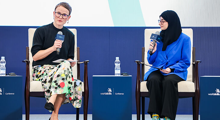 Zwei Frauen diskutieren auf der B&uuml;hne der WorldSkills Conference Shanghai 2026. Die Moderatorin links spricht in ein Mikrofon und h&auml;lt Notizen in der Hand.