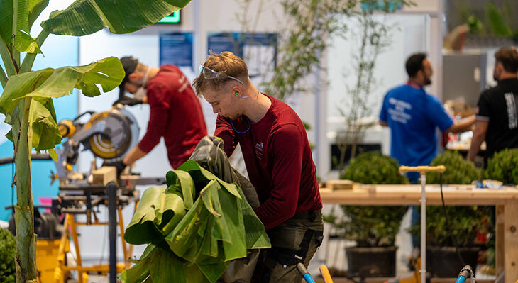 Ein deutscher Teilnehmer der WorldSkills Shanghai 2026 arbeitet konzentriert mit gro&szlig;en tropischen Pflanzenbl&auml;ttern im Wettbewerbsbereich Landschaftsg&auml;rtnerei.