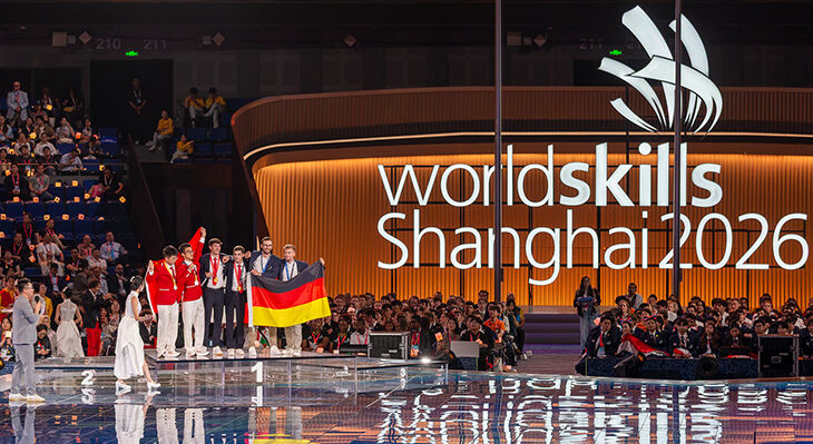 Deutsche Teilnehmende feiern bei der Siegerehrung der WorldSkills Shanghai 2026 auf dem Siegerpodest und pr&auml;sentieren eine Deutschlandflagge.
