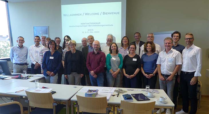 Gruppenfoto von 22 stehenden Menschen angeordnet in zwei Reihen in einem Konferenzraum