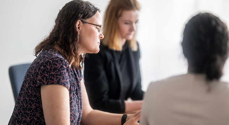 Drei Frauen sitzen an einem Tisch und unterhalten sich, zwei sind seitlich und eine von hinten zu sehen