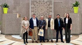 echs Personen stehen vor einer Wand mit aufwendigem Mosaikmuster und zwei gelben Blument&ouml;pfen auf Podesten