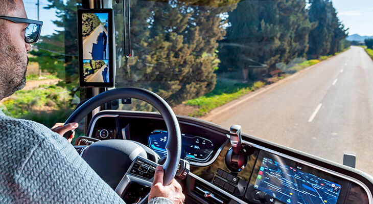 A lorry driver, photographed from the cab, is driving along a road through the countryside