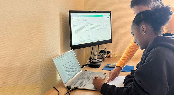 Zwei Personen sitzen an einem Tisch vor einem Laptop und einem externen Monitor