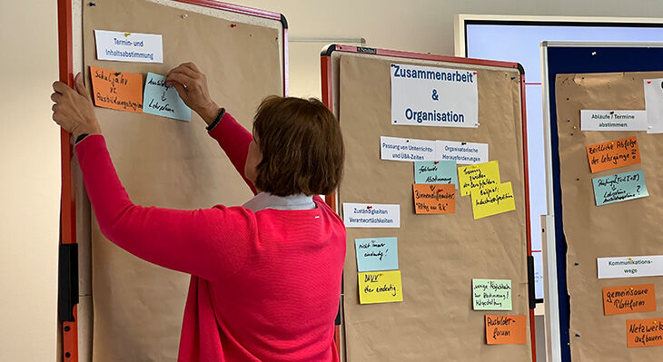 Eine Dame pinnt Zettel an eine Pinnwand zum Thema Zusammenarbeit und Organisation.