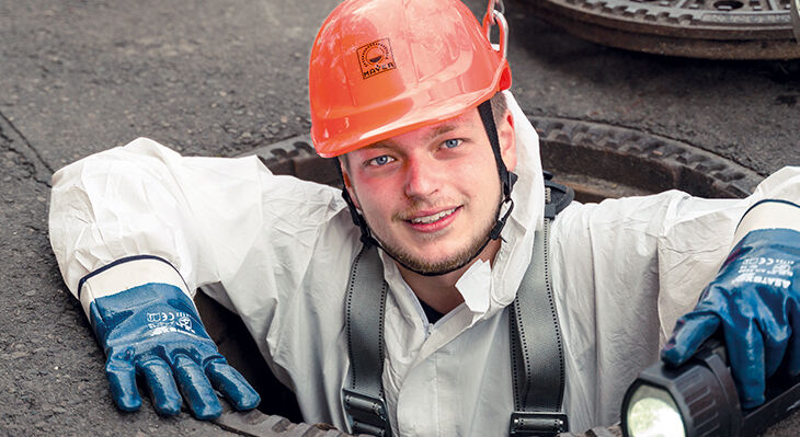 Ein Mann in Arbeitskleidung kommt aus einem Gulli.