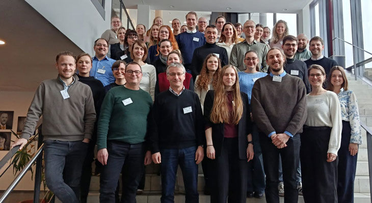 Gruppe von Personen steht auf einer Treppe in einem modernen Geb&auml;ude und posiert f&uuml;r ein Gruppenfoto