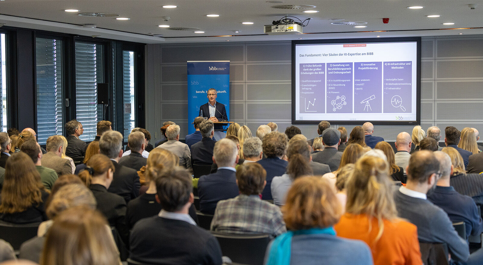 Gruppe von Personen in einem Raum, die sich vor einem Tisch mit Pflanzen unterhalten.