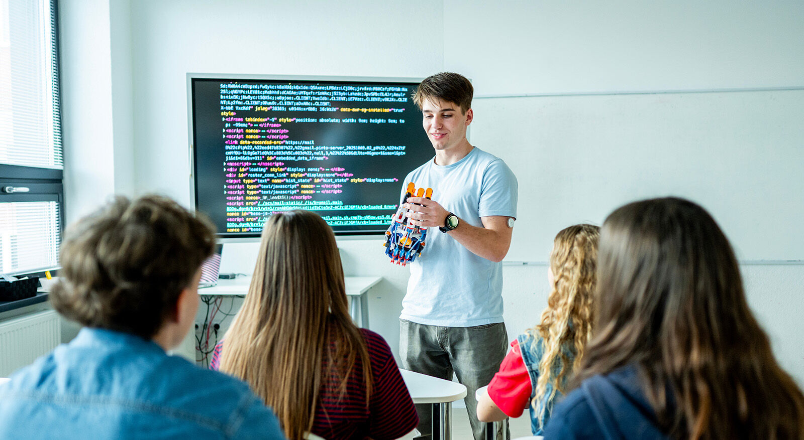 Junger Mann erkl&auml;rt ein Robotermodell vor einer Klasse