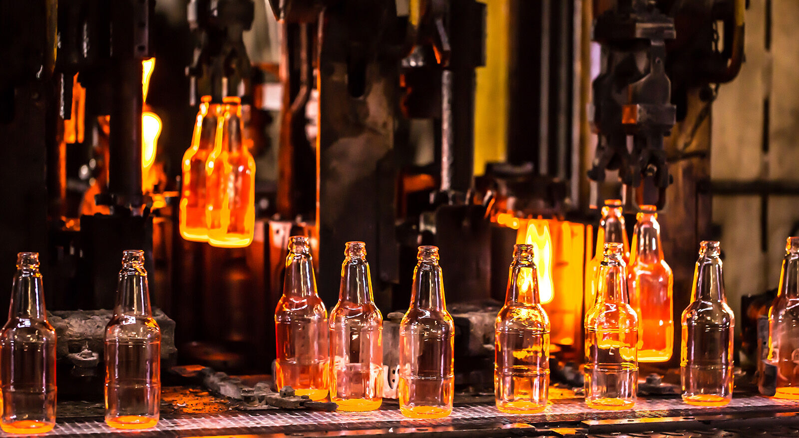 Flaschen aus geschmolzenem Glas werden in einer Fabrik auf einem F&ouml;rderband geformt und abgek&uuml;hlt.