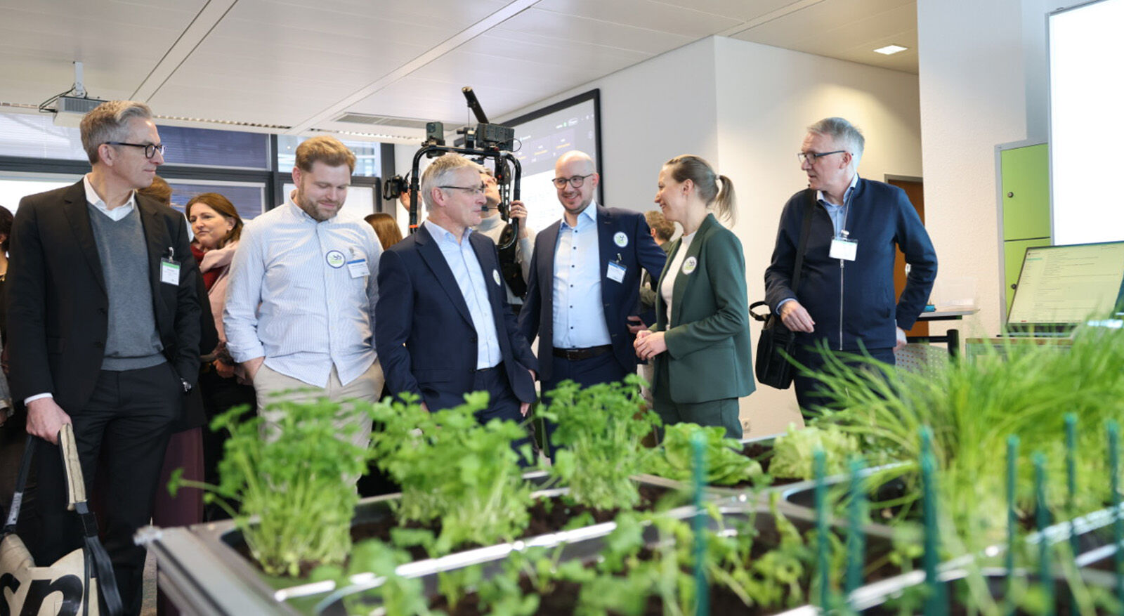 Gruppe von Personen in einem Raum, die sich vor einem Tisch mit Pflanzen unterhalten.