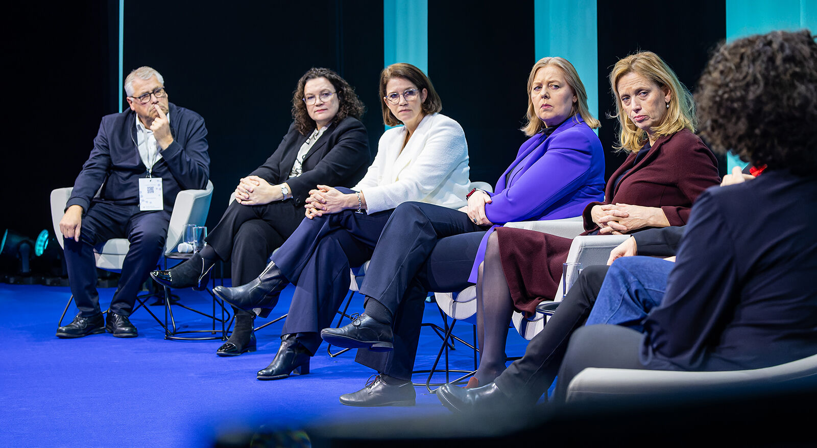 Ein Mann und vier Frauen sitzen nebeneinander auf einem Diskussionspanel. Im Vordergrund sieht man die Moderatorin von hinten.