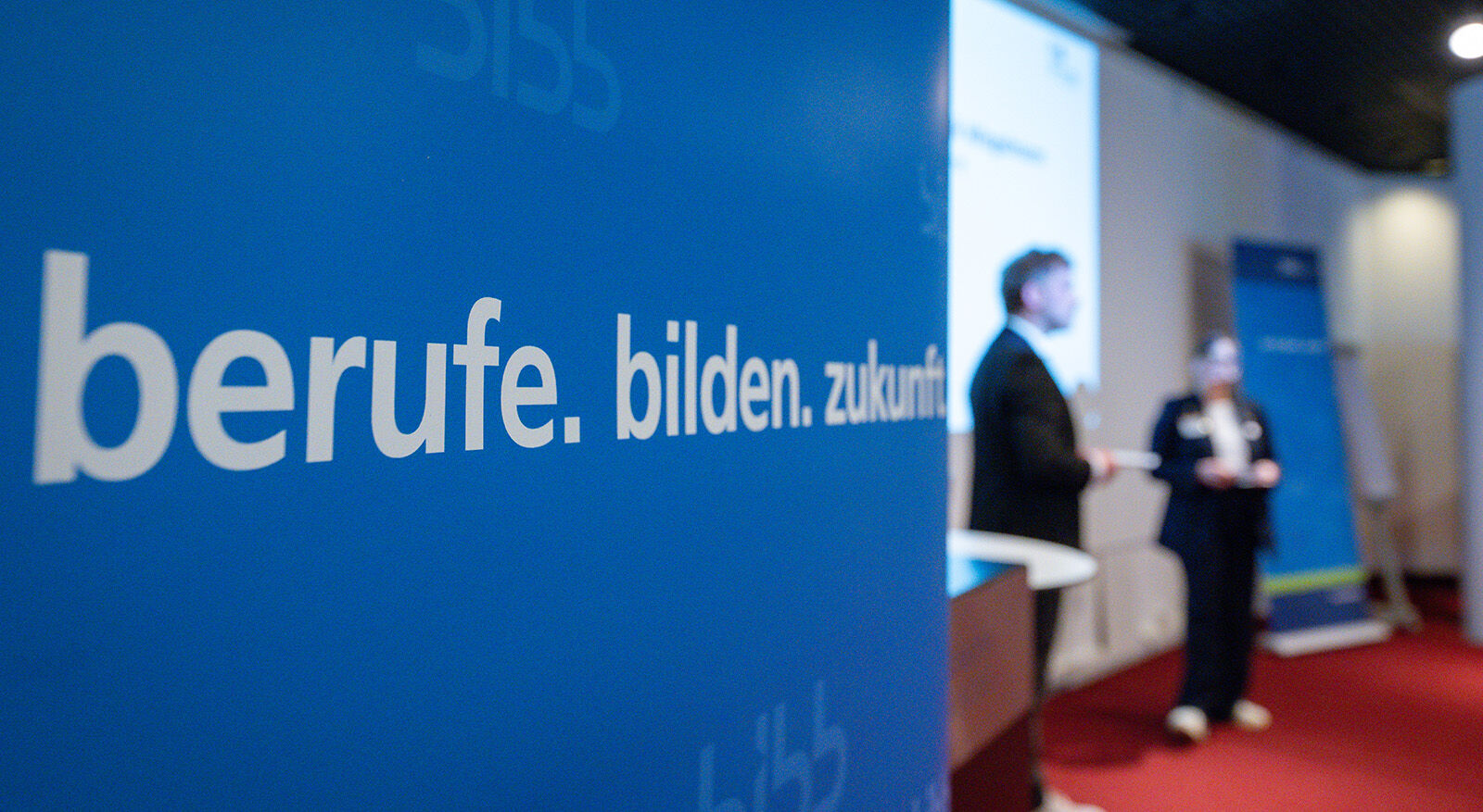Links Plakat mit dem Slogan "berufe bilden zukunft", im rechten Bildteil sind verschwommen Menschen zu sehen.