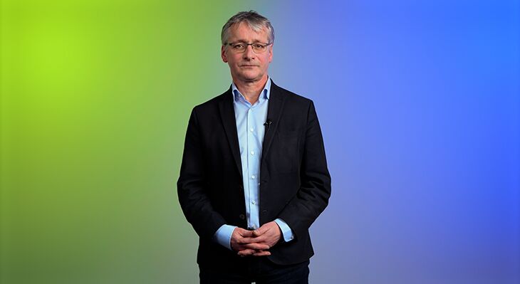 Mr. Ertl speaking in front of a green and blue background.
