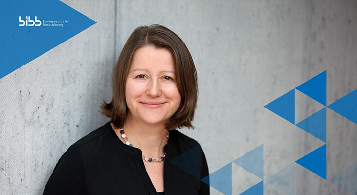 Porträt einer lächelnden Frau vor einer grauen Betonwand. Sie trägt eine schwarze Bluse und eine Halskette. Oben links ist das Logo des Bundesinstituts für Berufsbildung zu sehen; rechts sind blaue Dreiecksformen eingeblendet.